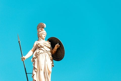 Statue of Athena holding a spear and shield, set against a clear blue sky.