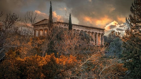 View of the Temple of Hephaestus in Athens at sunset, surrounded by autumn trees and illuminated by warm evening light.