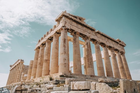 Low-angle view of the Parthenon on the Acropolis in Athens, Greece, showing its Doric columns and ancient marble structure against a bright sky.