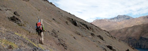 Student with backpack of supplies hiking on steep mountainside in Chile