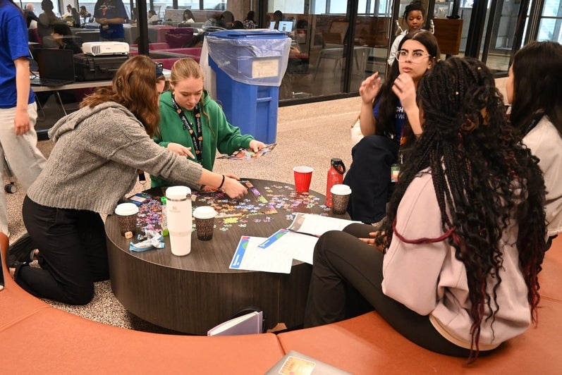 participants sitting around a table, some are talking while others are working on a puzzle on the table
