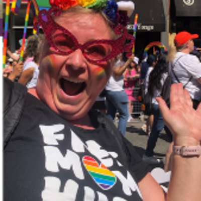 Picture of Judith Koeller at a Pride Event wearing a rainbow flower headband and a black tshirt that says "Free Mom Hugs Southern Ontario" 