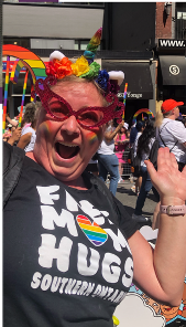 Picture of Judith Koeller at a Pride Event wearing a rainbow flower headband and a black tshirt that says "Free Mom Hugs Southern Ontario" 