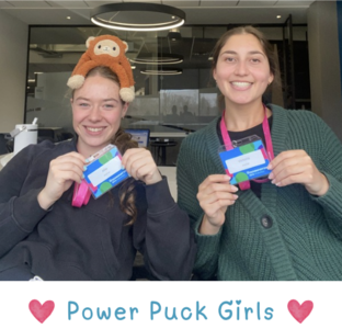 Power Puck Girls two team members (the girls on the left has a stuffed monkey on their head) holding up their Technovation Waterloo Lanyards. "Power Puck Girls" in two heart emojis is written below the image