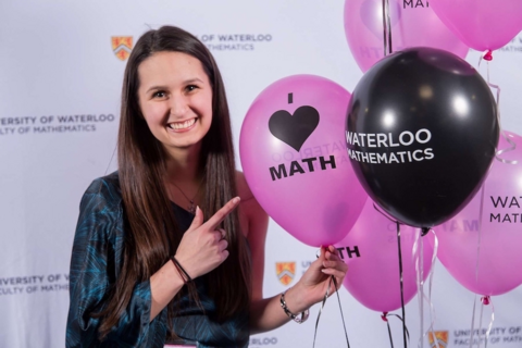 Female student smiling and pointing at pink and black math balloons