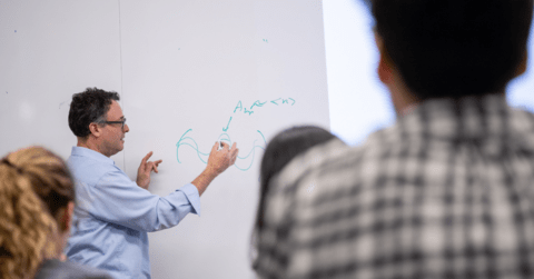 Professor writing on white board in front of students