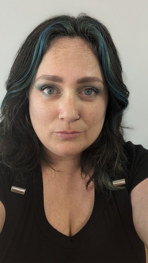 Meghan Ashdown. She has shoulder-length brown and blue hair and blue eyes, and is wearing a black top. She is looking directly at the camera with a neutral face.