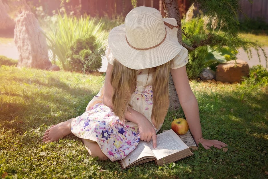 Girl sitting on grass and reading a book in the sun 
