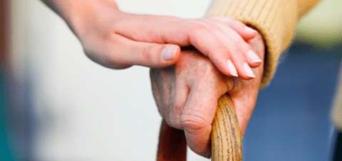 Young person holding older person's hand with cane.