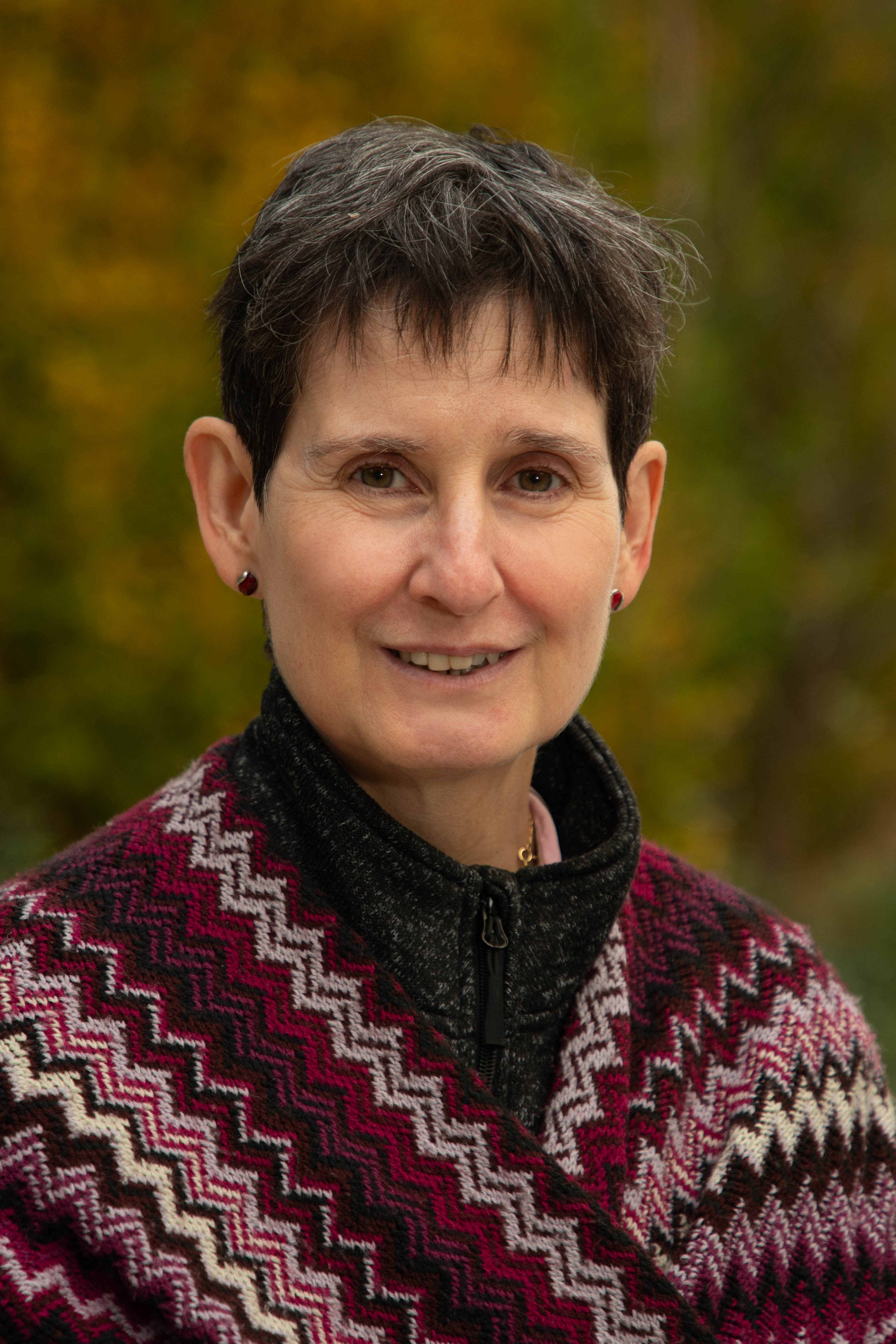 Photo of Ana Ferrer, wearing a patterned shawl, set against a blurred autumn outdoor background.